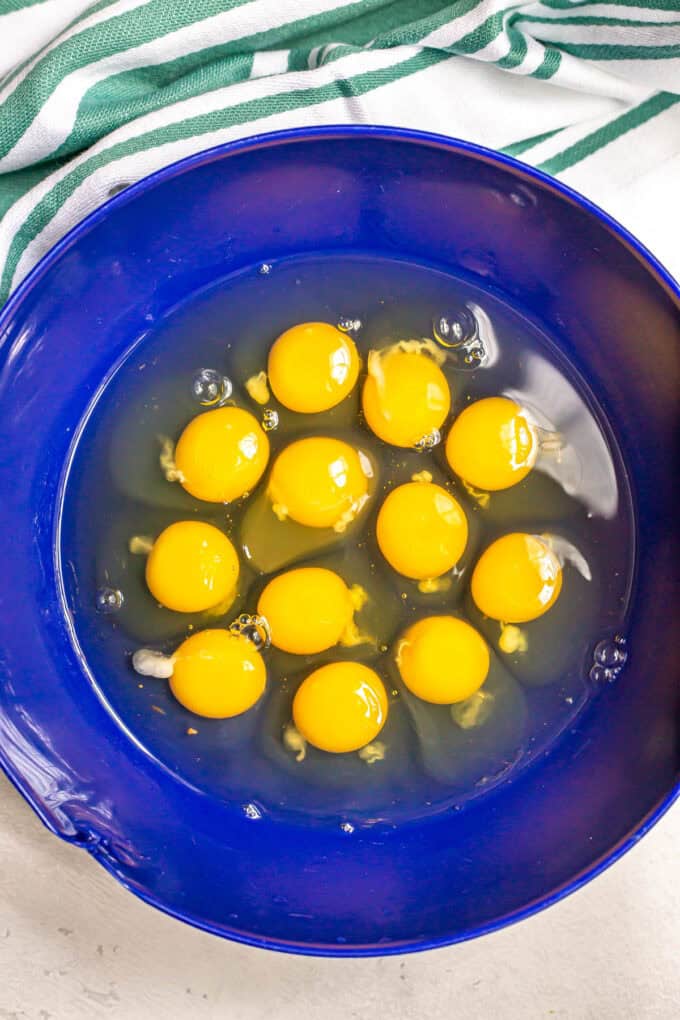 A dozen eggs in a big blue bowl before being whisked together.