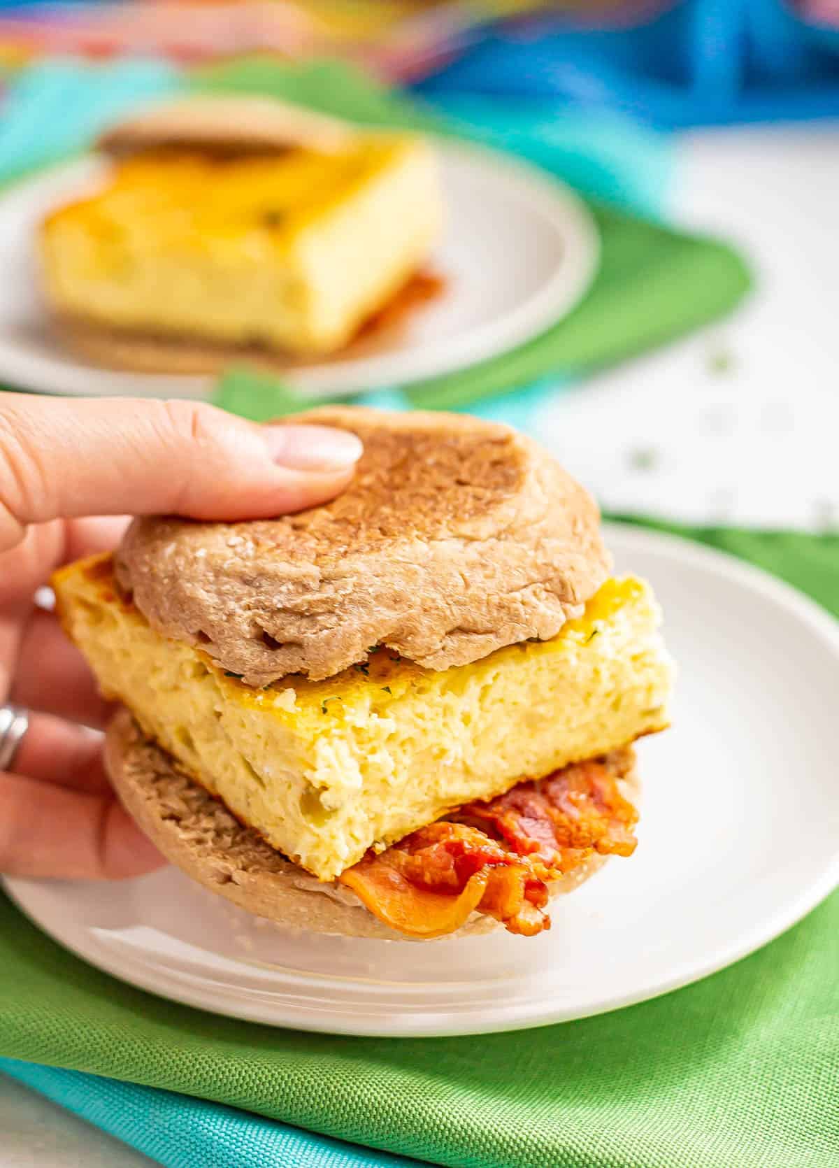 A hand holding up a breakfast sandwich with bacon and baked eggs.