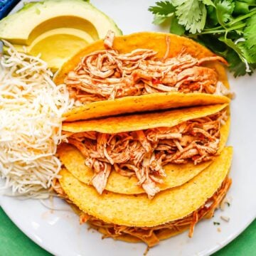 Close up of a trio of crunchy taco shells stuffed with seasoned shredded chicken mixed with salsa.
