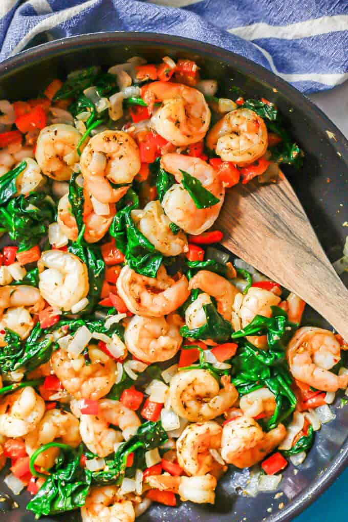 A wooden spatula resting in a pan with a shrimp and veggie mixture.