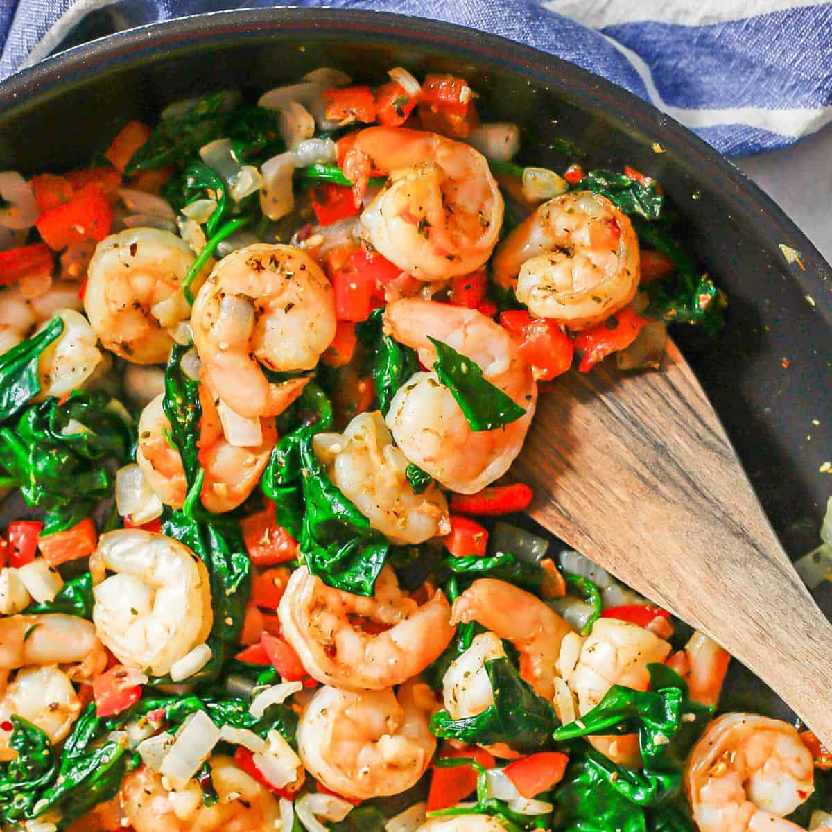 Close up of a wooden spatula resting in a pan with a shrimp and veggie mixture.