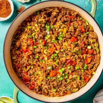 Close up of one pot Cajun dirty rice cooked in a green Dutch oven pot with sliced green onions on top.