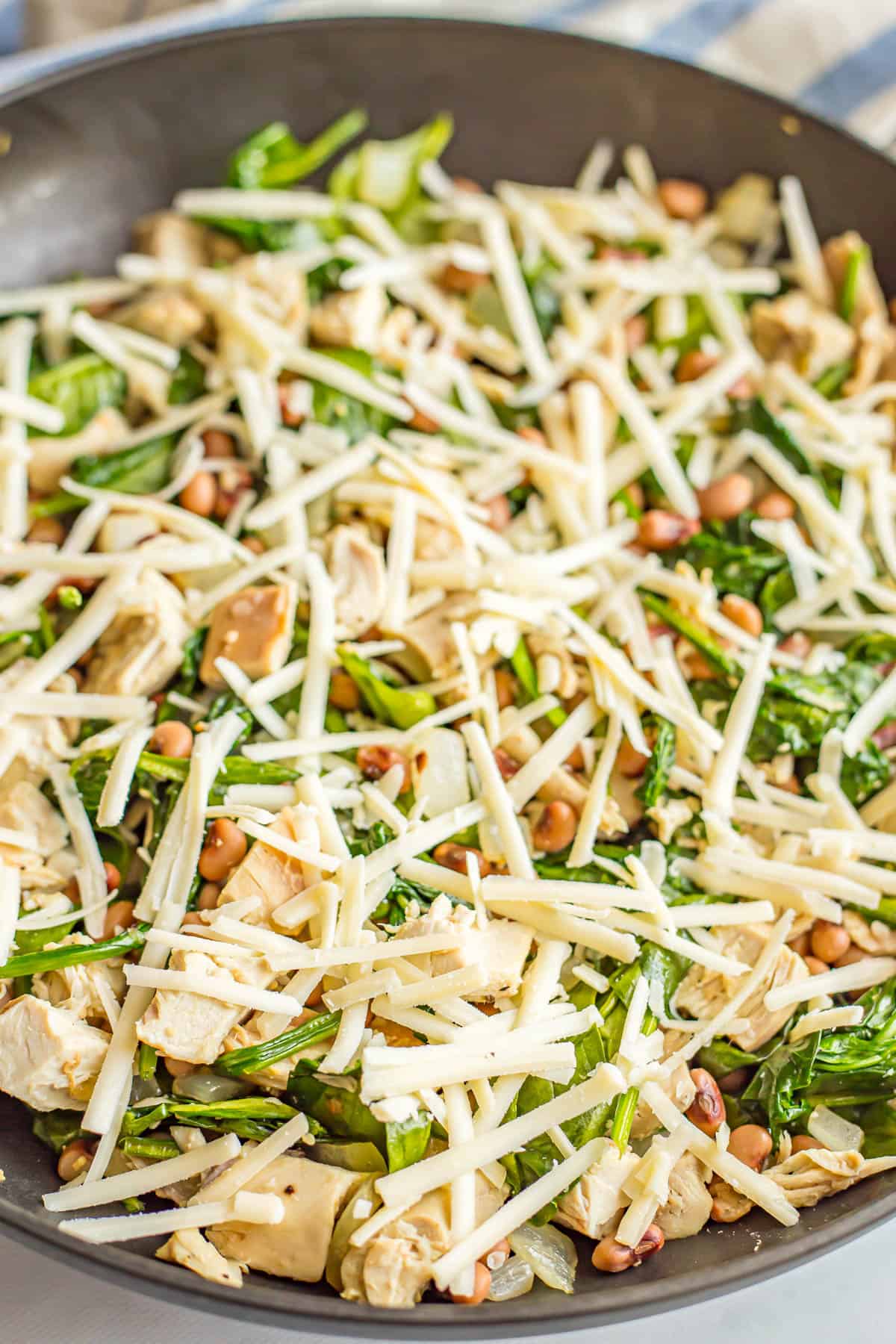 Shredded cheese on top of a mixture of chicken, field peas and spinach in a large skillet.