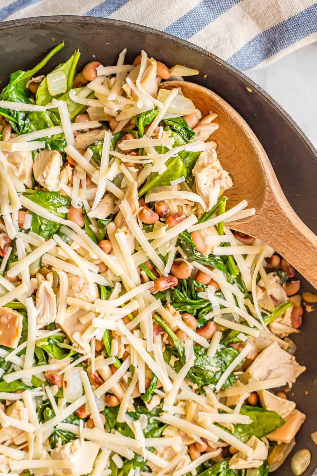 A wooden spoon resting in a skillet of a one pot wonder recipe with chicken, beans and spinach.