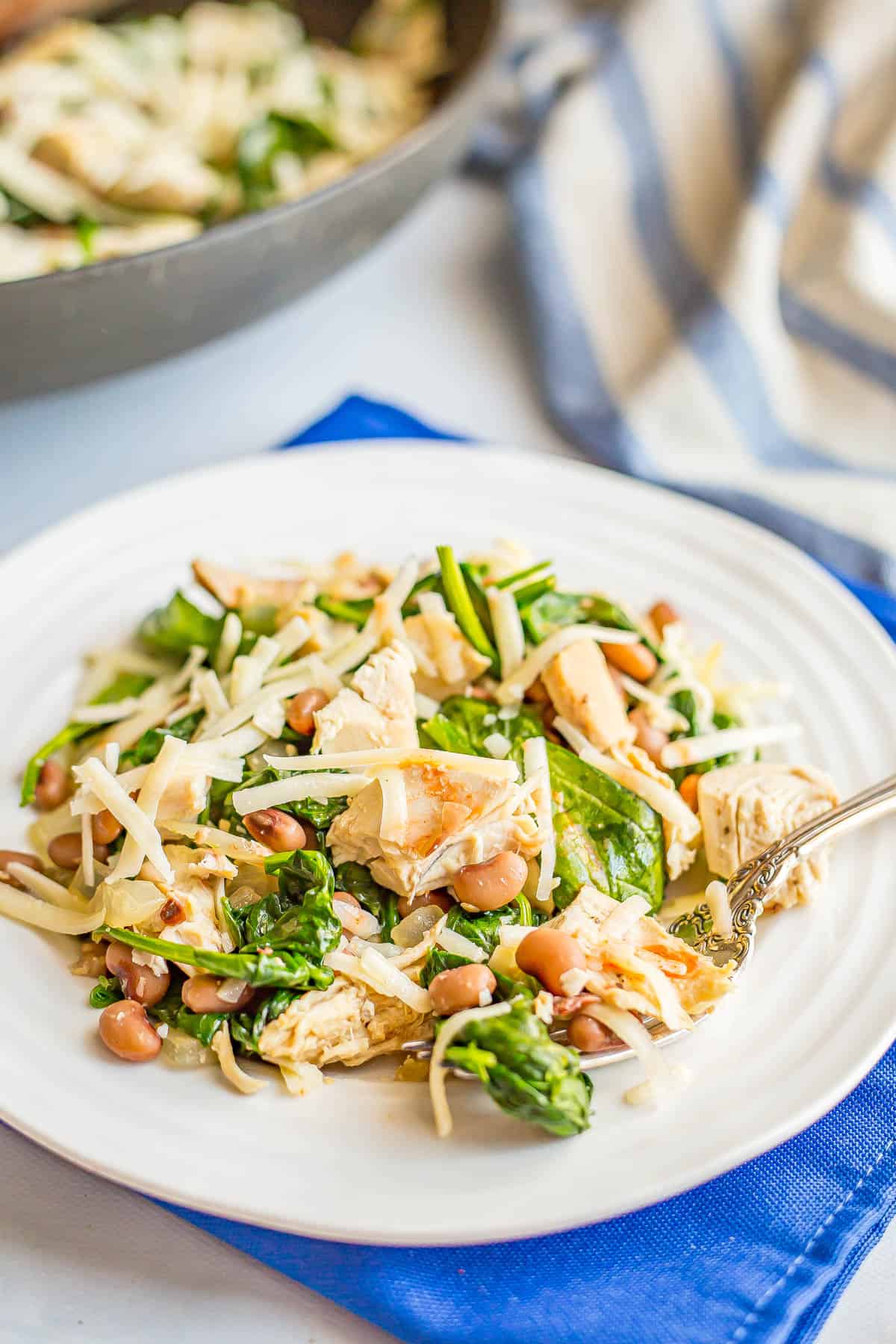 A white dinner plate with a chicken, field peas and spinach mixture topped with cheese.
