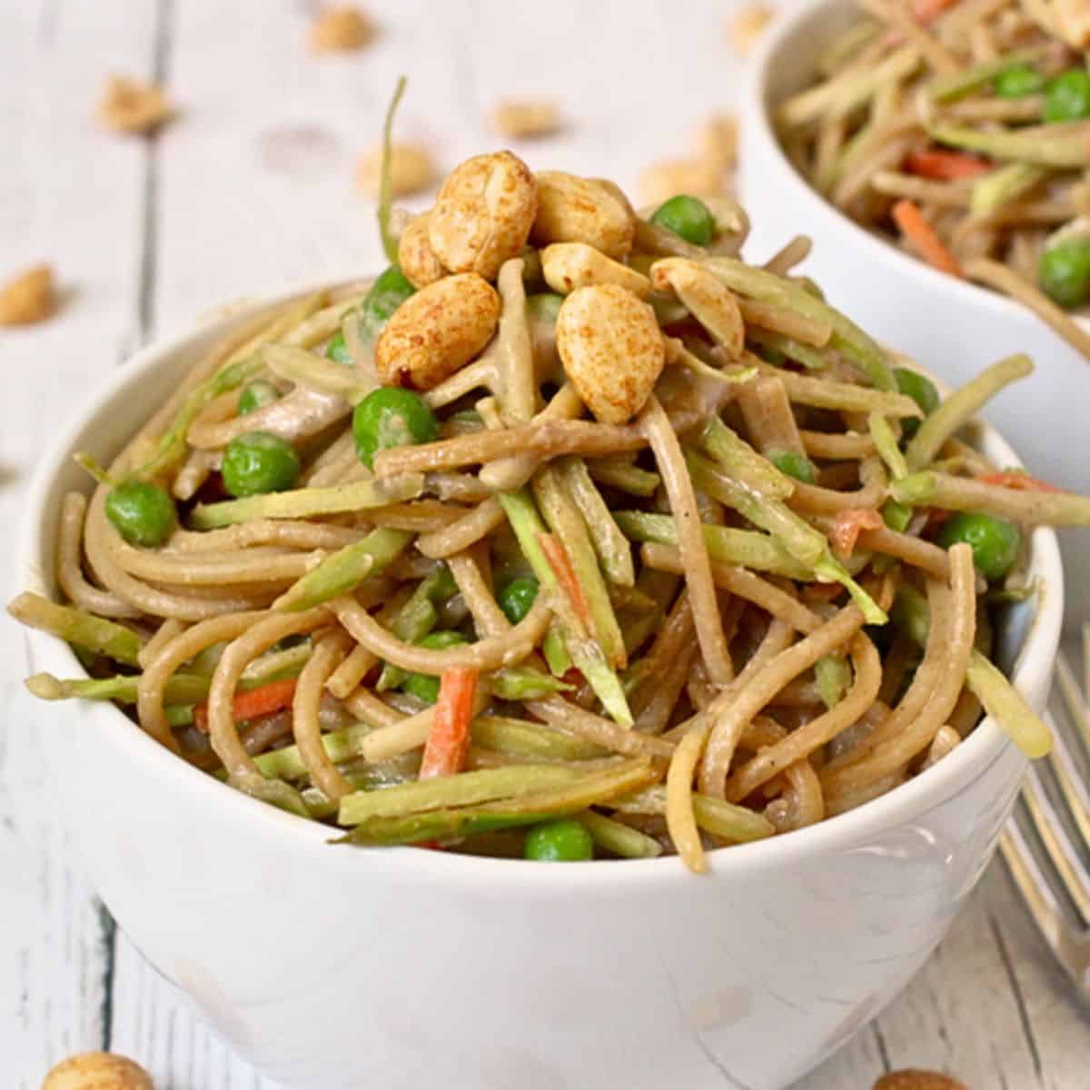 Close up of a white bowl with a swirl of peanut butter spaghetti with vegetables and peanuts sprinkled on top.
