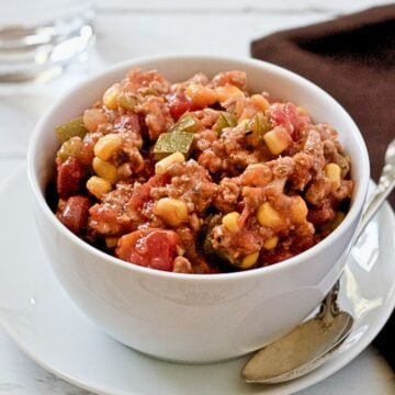 Close up of a small white bowl with a ground turkey and vegetable stew and a spoon to the side.