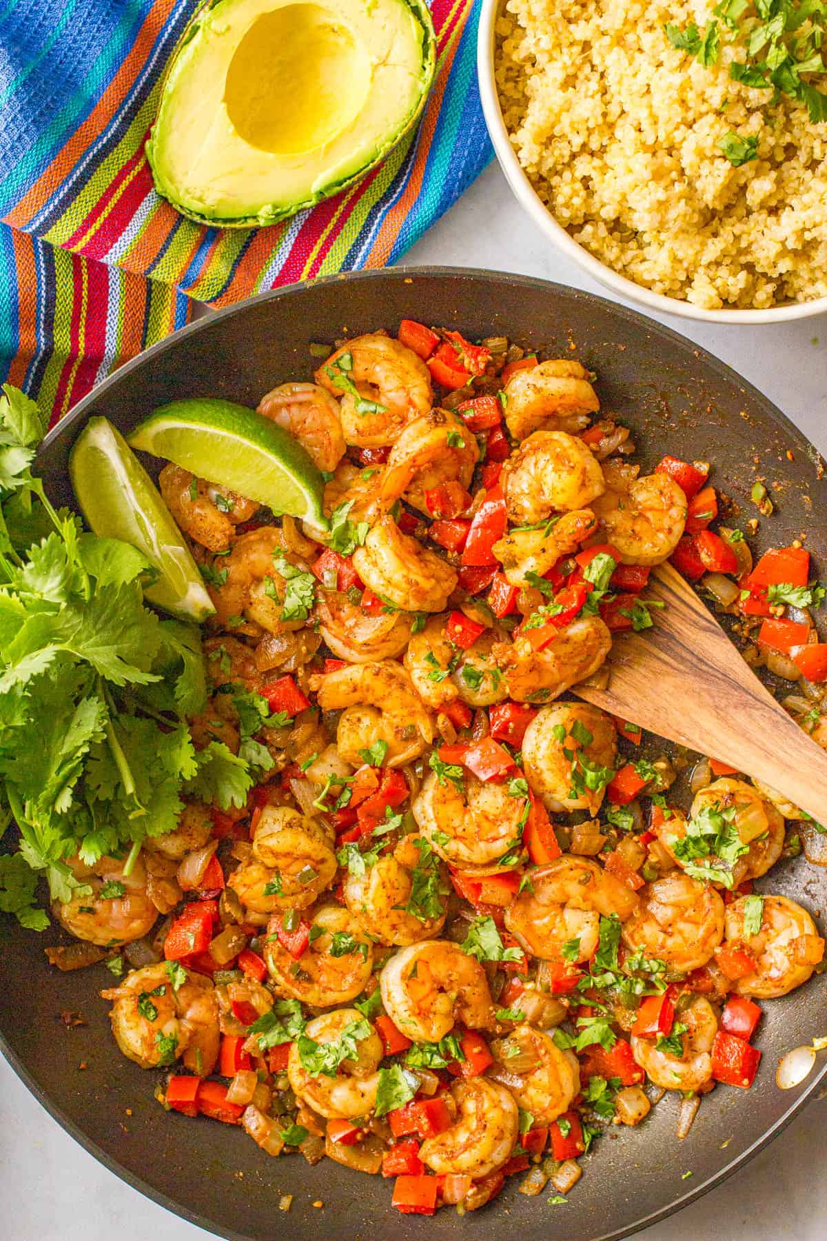A wooden spatula resting in a large pan with a shrimp and pepper mixture topped with cilantro.