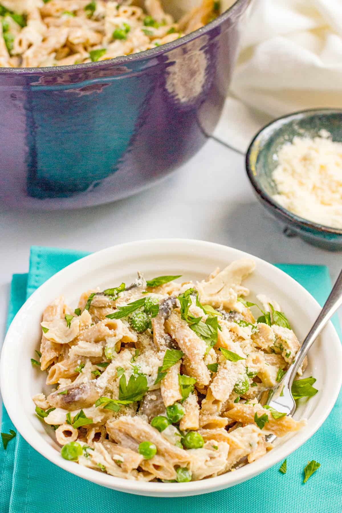 A bowl full of a chicken and mushroom pasta topped with fresh parsley and sitting on a teal napkin.