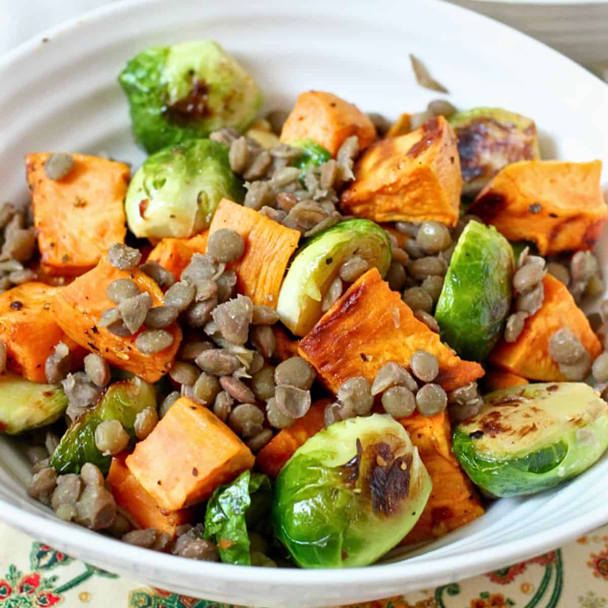 Close up of a bowl with a mixture of roasted sweet potatoes and Brussels sprouts with brown lentils.