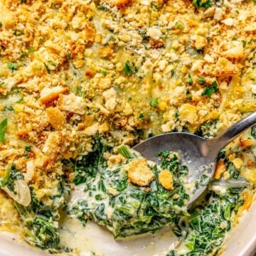 Close up of a spoon scooping out a bit of creamed spinach casserole from a baking dish.