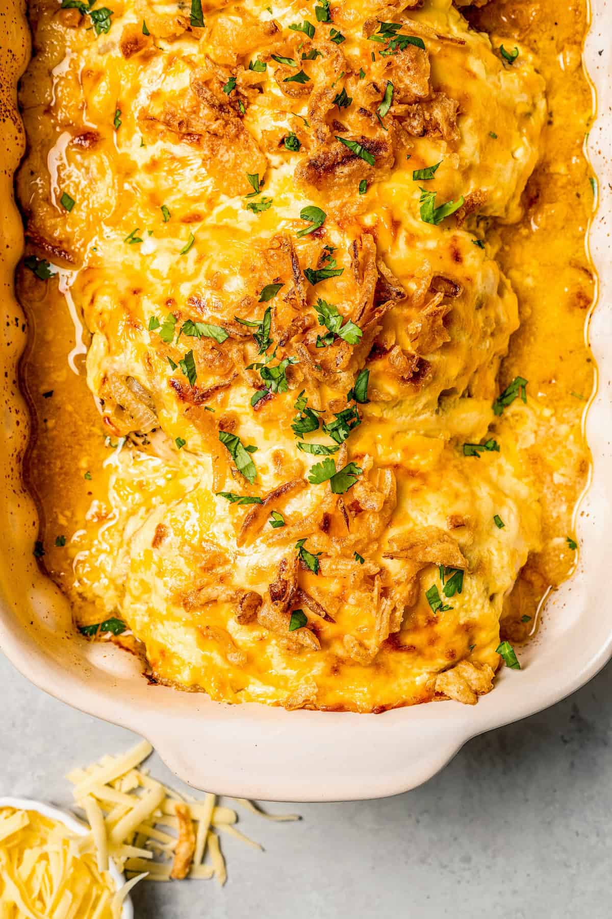 Close up of baked creamy chicken breasts with French fried onions on top in a casserole dish.