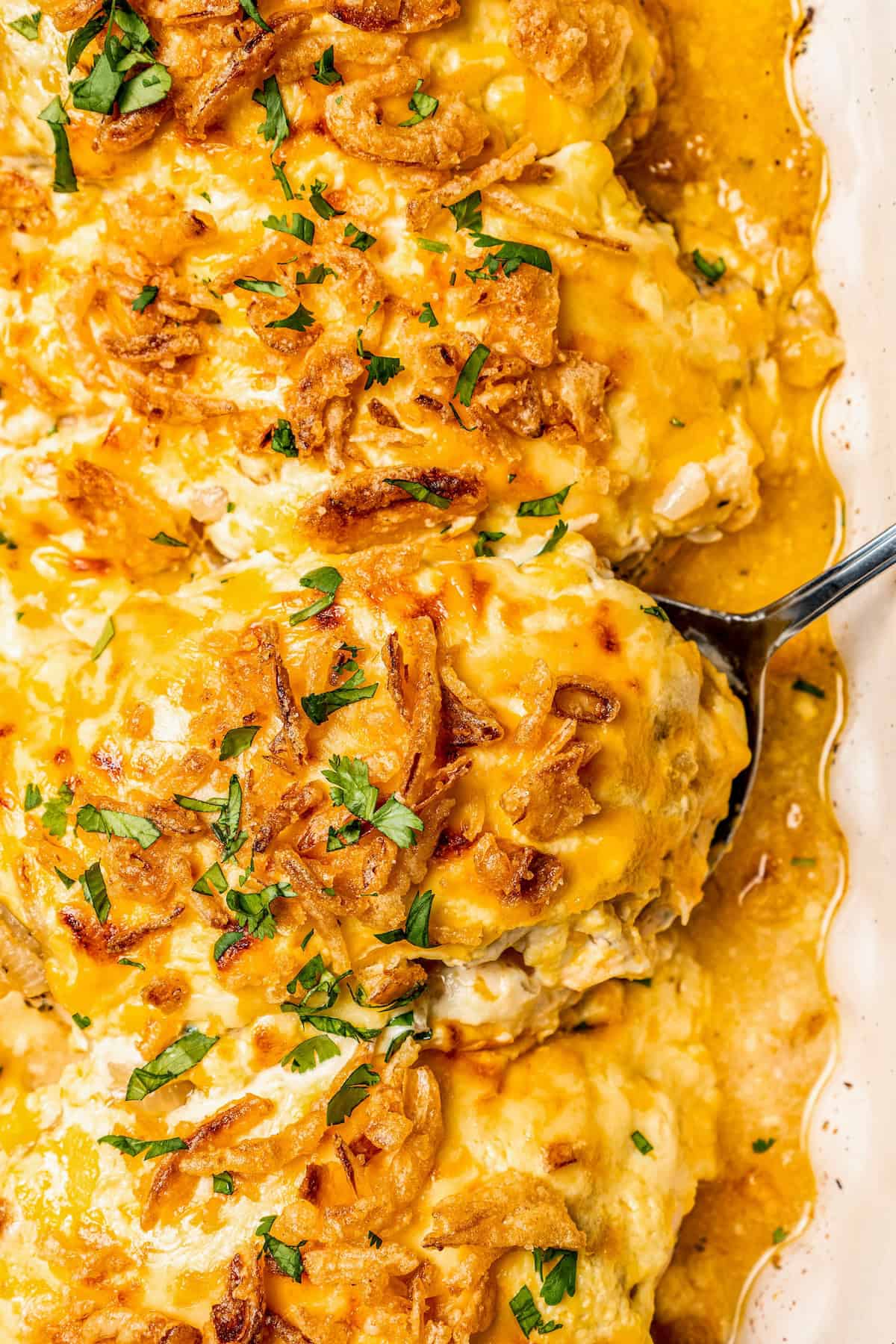 A spoon lifting up baked French onion chicken from a casserole dish.