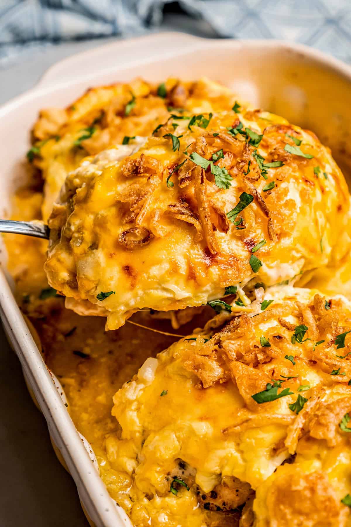 A serving spoon lifting out a chicken breast topped with caramelized onions from a casserole dish.