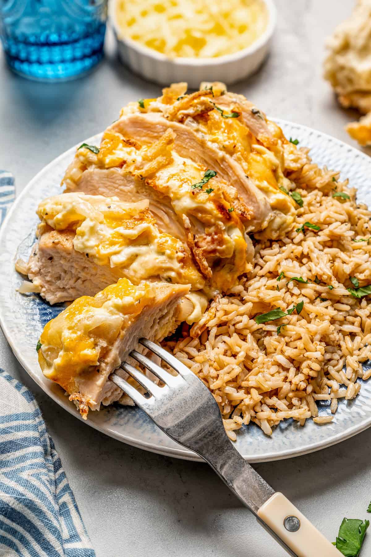 A fork resting in a slice of French onion baked chicken alongside brown rice on a round blue dinner plate.