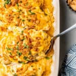 A big spoon resting in a rectangular baking dish of a French onion chicken casserole with a text overlay on the photo.