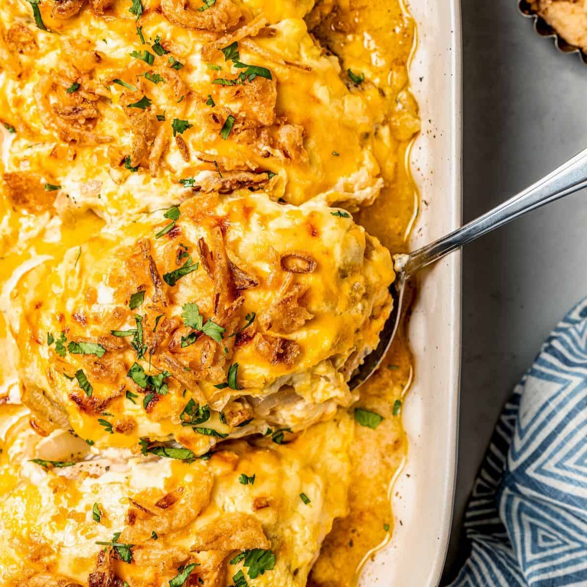 Close up of a spoon lifting a baked creamy French onion chicken breast from a baking dish.