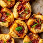 Close up of mini baked brie bites with pecans, bacon and other toppings and sprigs of fresh herbs for garnish and a text overlay on the photo.