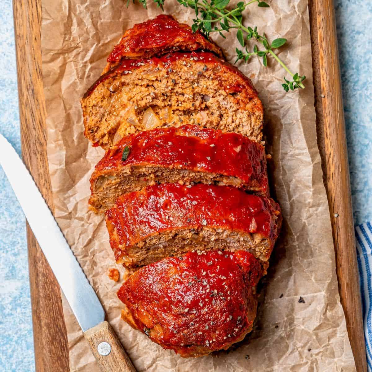 Close up of a sliced mini turkey meatloaf on a small wooden cutting board with sprigs of thyme nearby.