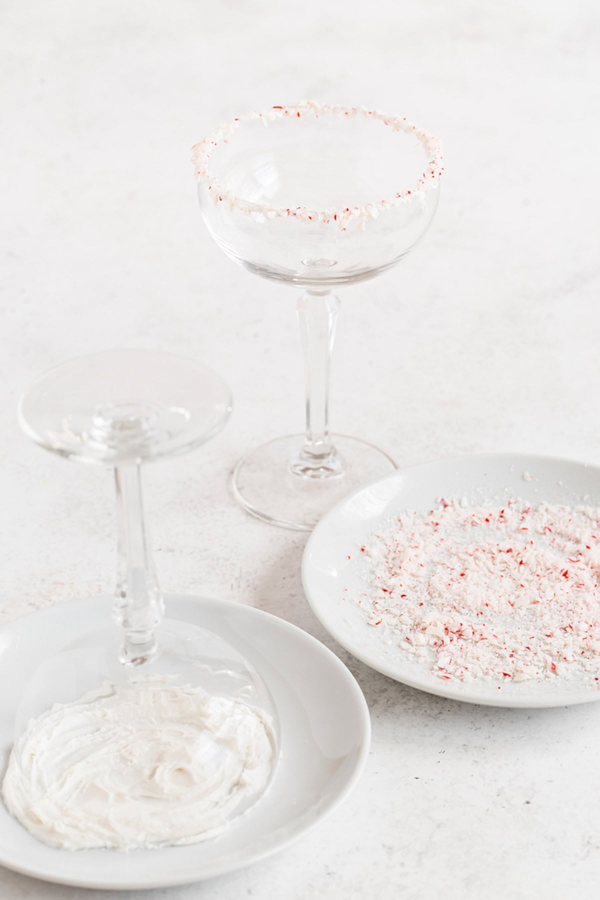 Two coupe glasses being rimmed with crushed peppermint.