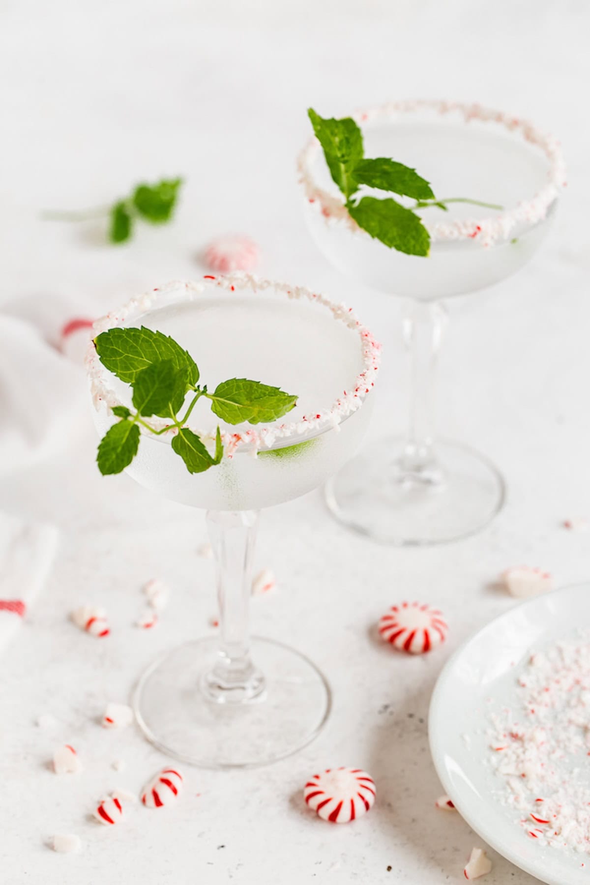 Two clear martinis served in glasses with crushed peppermint rims and sprigs of mint for garnish.