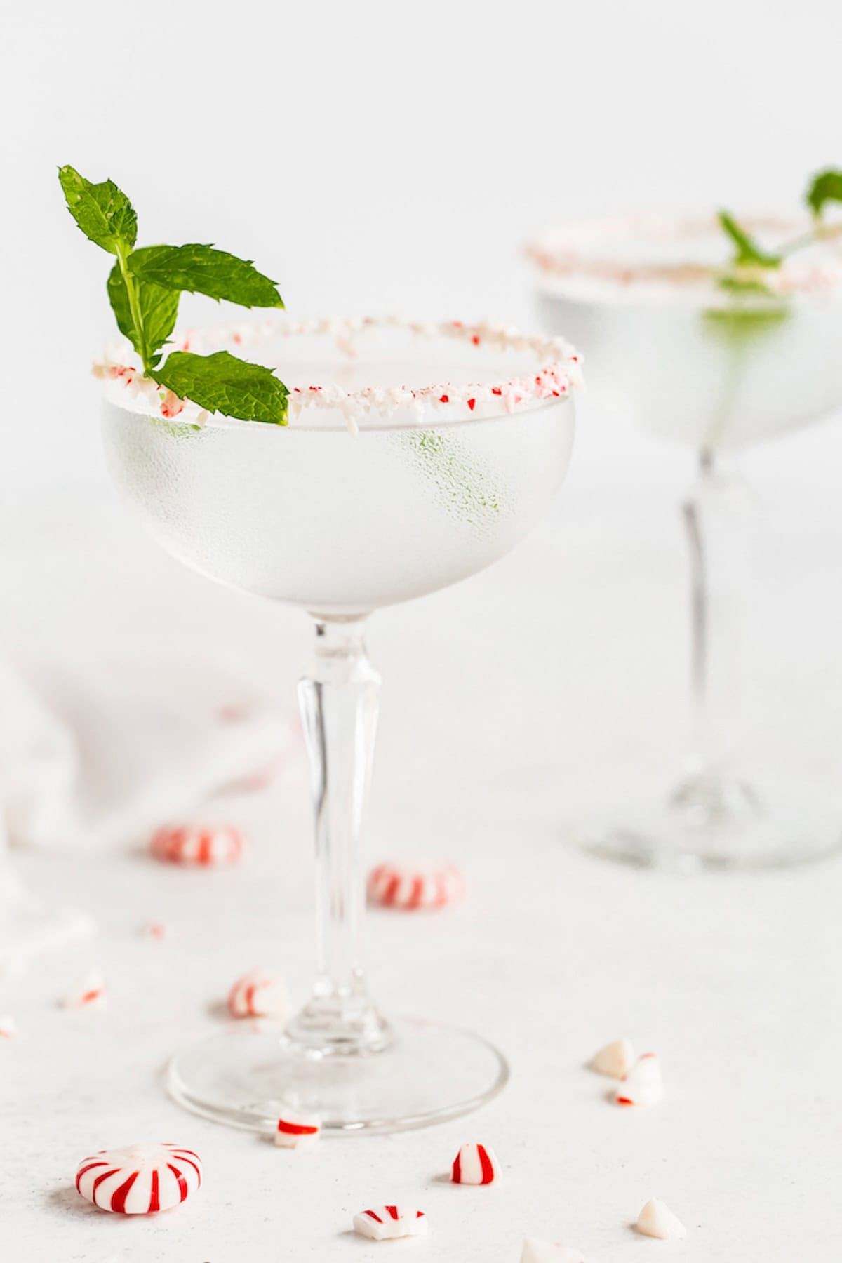 Peppermint flavored martinis in glasses rimmed with crushed peppermint pieces and garnished with lime.