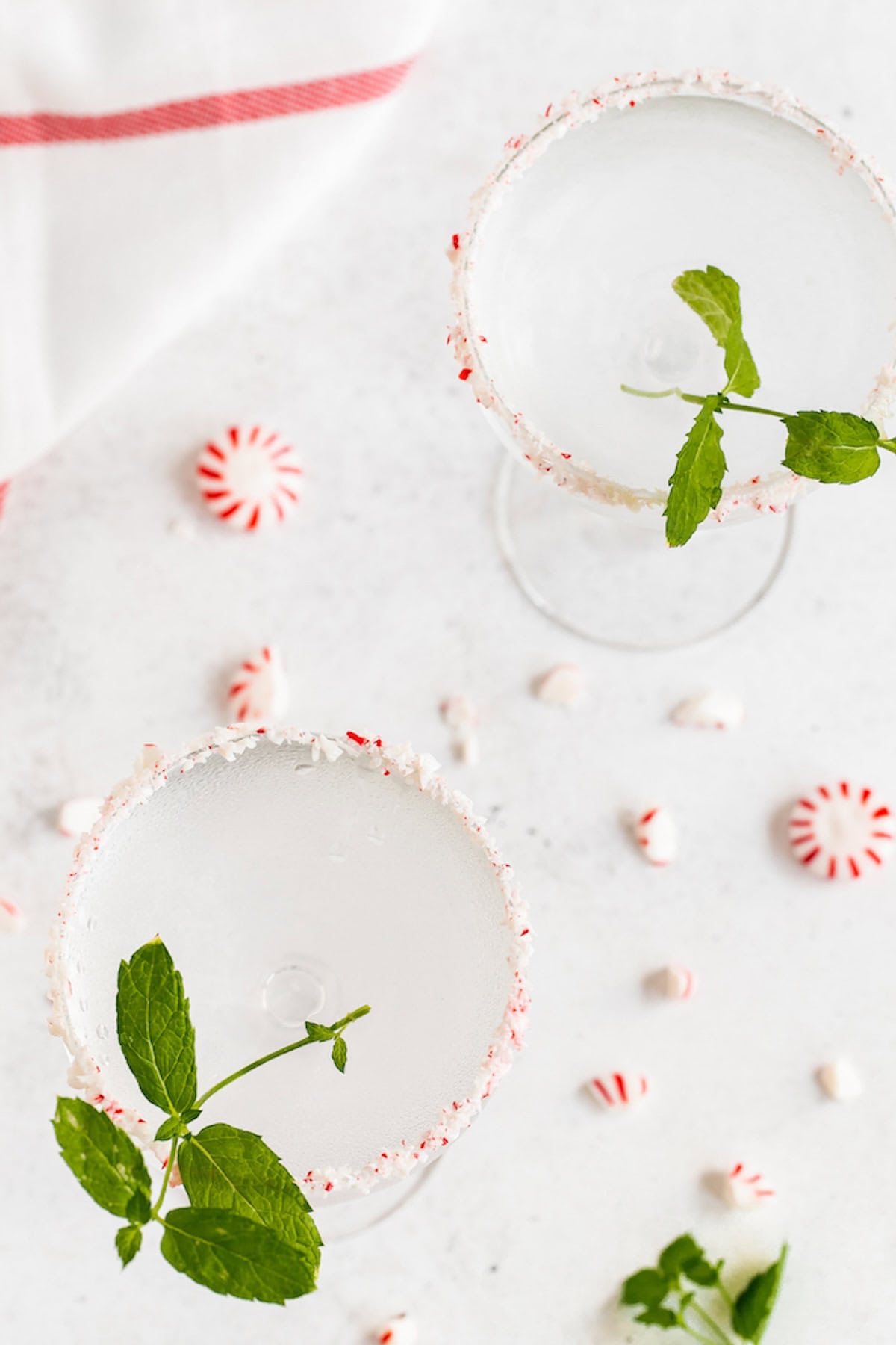 Overhead of peppermint martinis in clear coupe glasses with peppermint candies scattered around the glasses.