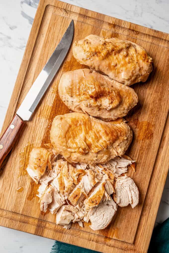 Chicken breasts resting on a wooden cutting board before being sliced.