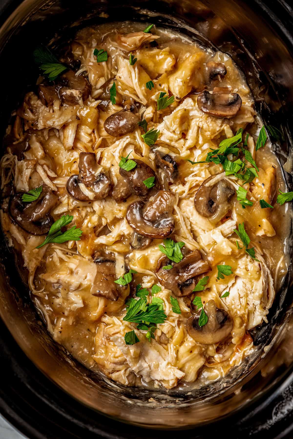 Slow cooker chicken marsala with mushrooms in a dark crock pot insert.
