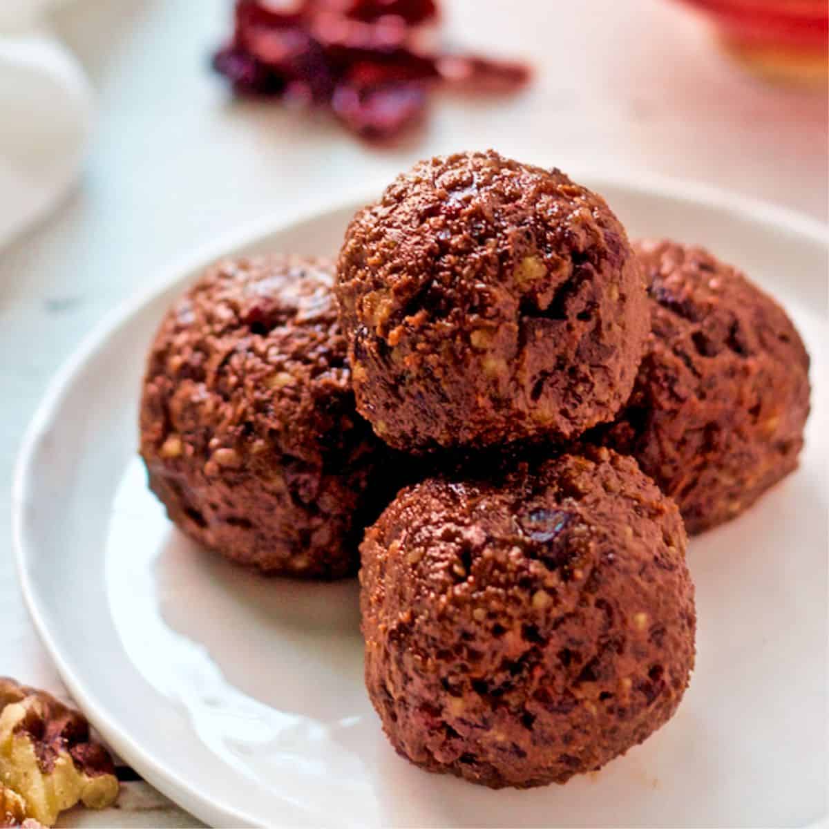 Close up of raw cranberry chocolate energy balls stacked on a small white plate.
