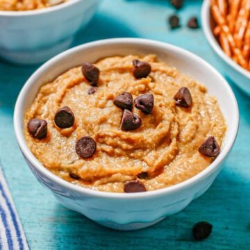 Close up of a bowl of chickpea cookie dough with chocolate chips on top and to the side.