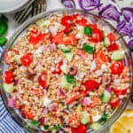Mediterranean farro salad with olives and feta cheese in a large glass bowl with colorful throw towels nearby and a text overlay on the photo.