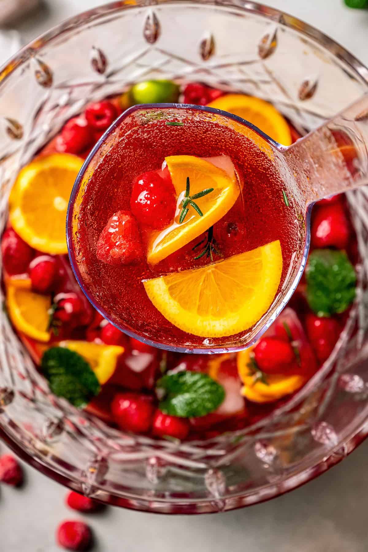 A ladle holding up a serving of a red punch with fresh fruit.