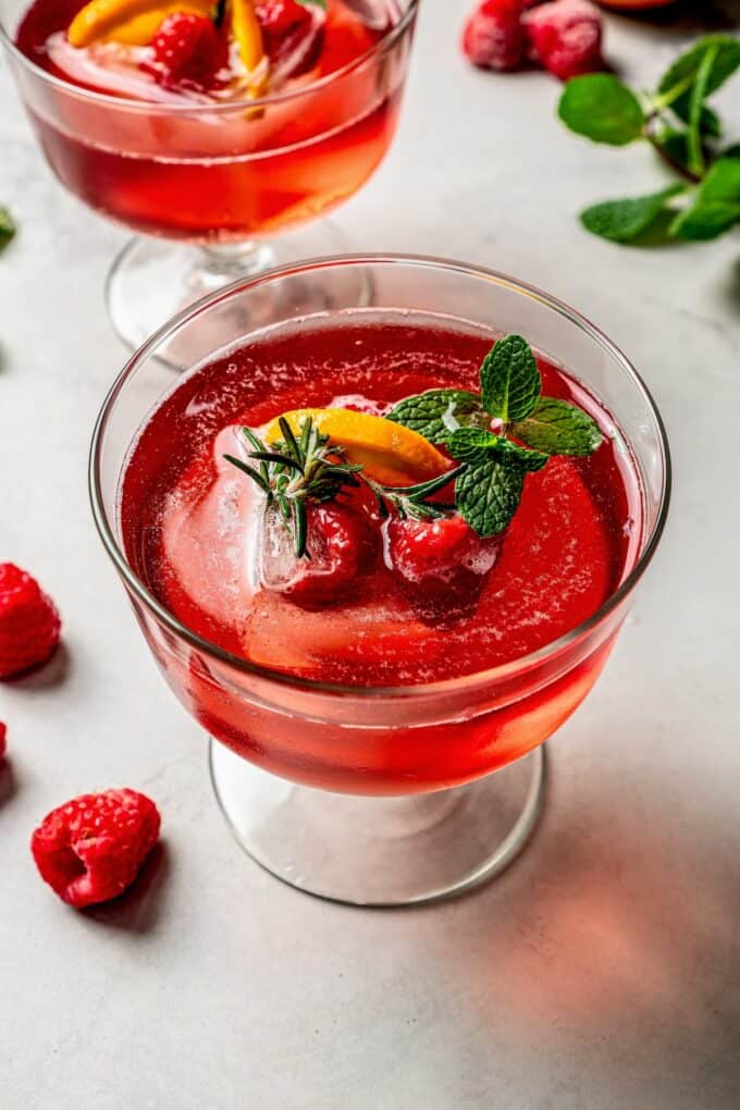 A coupe glass with a red Christmas punch topped with fresh fruit and mint sprigs.