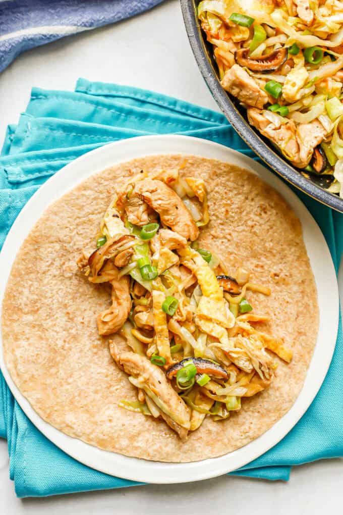A white plate with a tortilla topped with a mixture of chicken and cabbage.