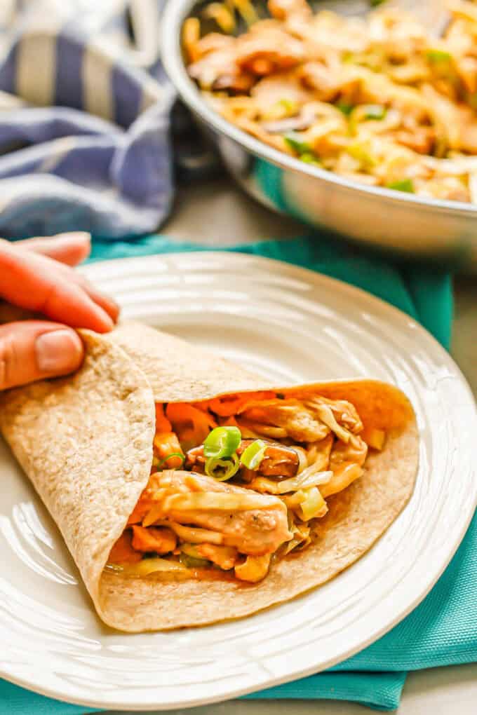 A hand wrapping a tortilla around a mixture of chicken and cabbage.