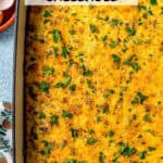 Baked grits and sausage casserole in a large baking dish with chopped fresh parsley on top and a text overlay on the photo.