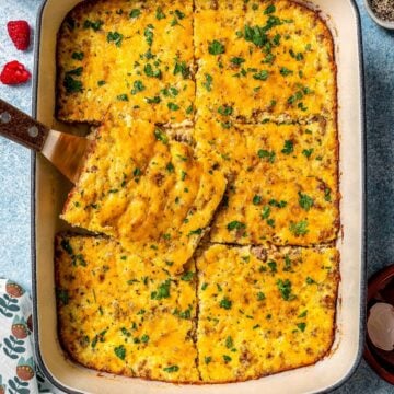 Close up of a small spatula lifting out a piece of sausage grits casserole from a baking dish.