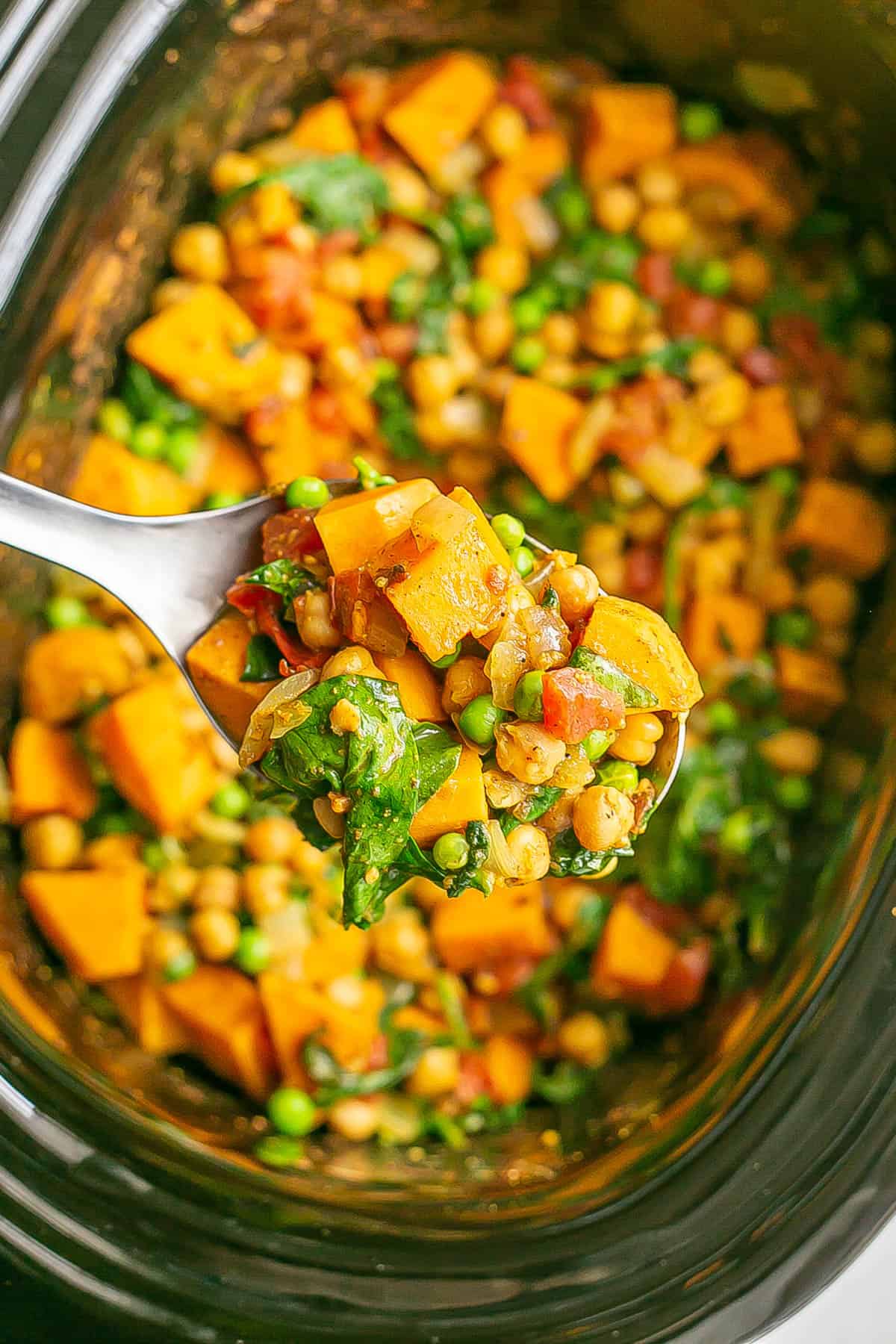 A serving spoon scooping up vegetarian curry from a slow cooker.