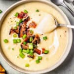 A spoon resting in a bowl of loaded potato soup with bacon and green onions on top and a text overlay on the photo.
