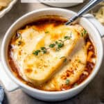 A bowl of French onion soup topped with bread and melty cheese with a spoon resting in it and a text overlay on the photo.