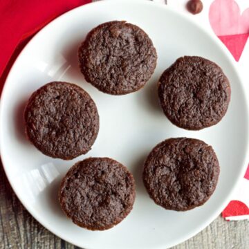 Five healthy double chocolate mini cupcakes without frosting on a white plate with red and pink napkins to the side.