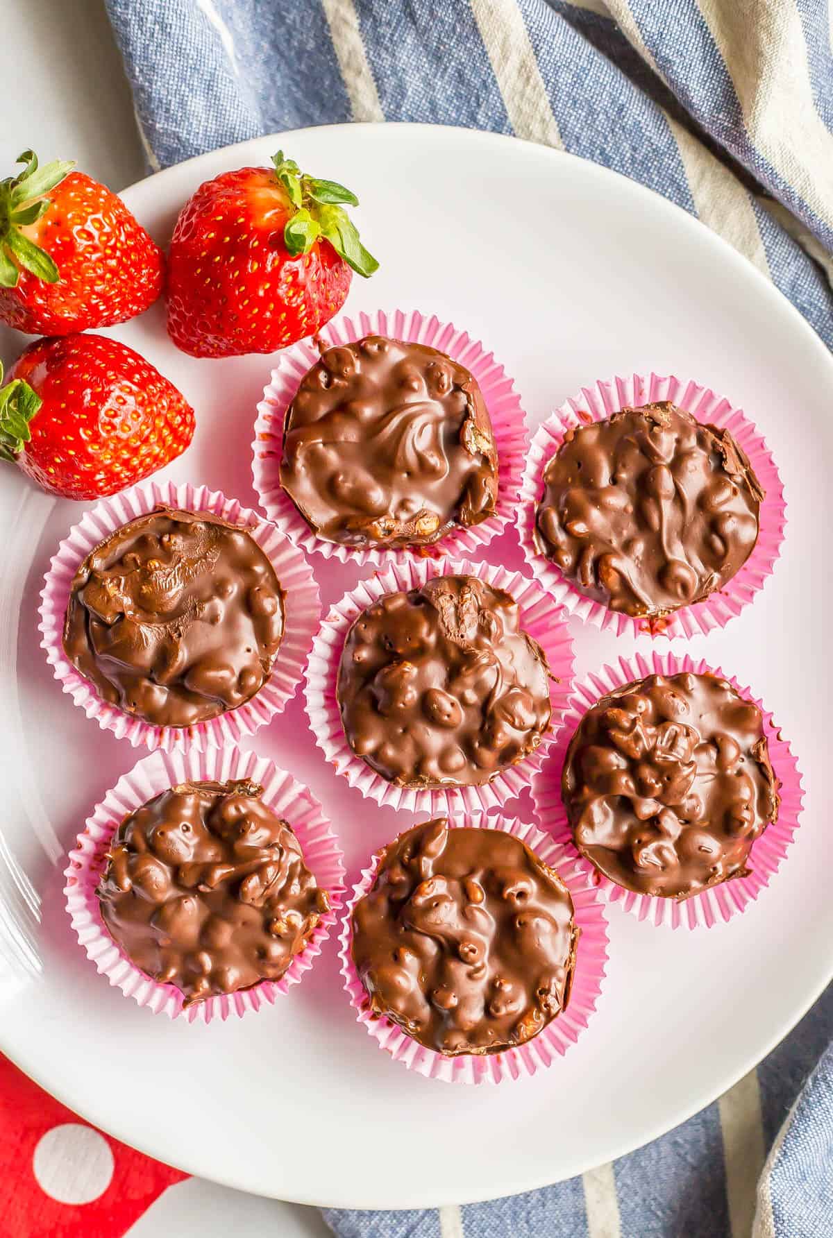 Seven mini homemade chocolate candies in pink cupcake liners on a white plate with strawberries to the side.