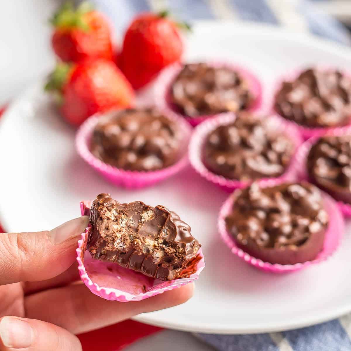 A hand holding a piece of chocolate candy with a bite taken out of it resting in a pink mini muffin paper cup.