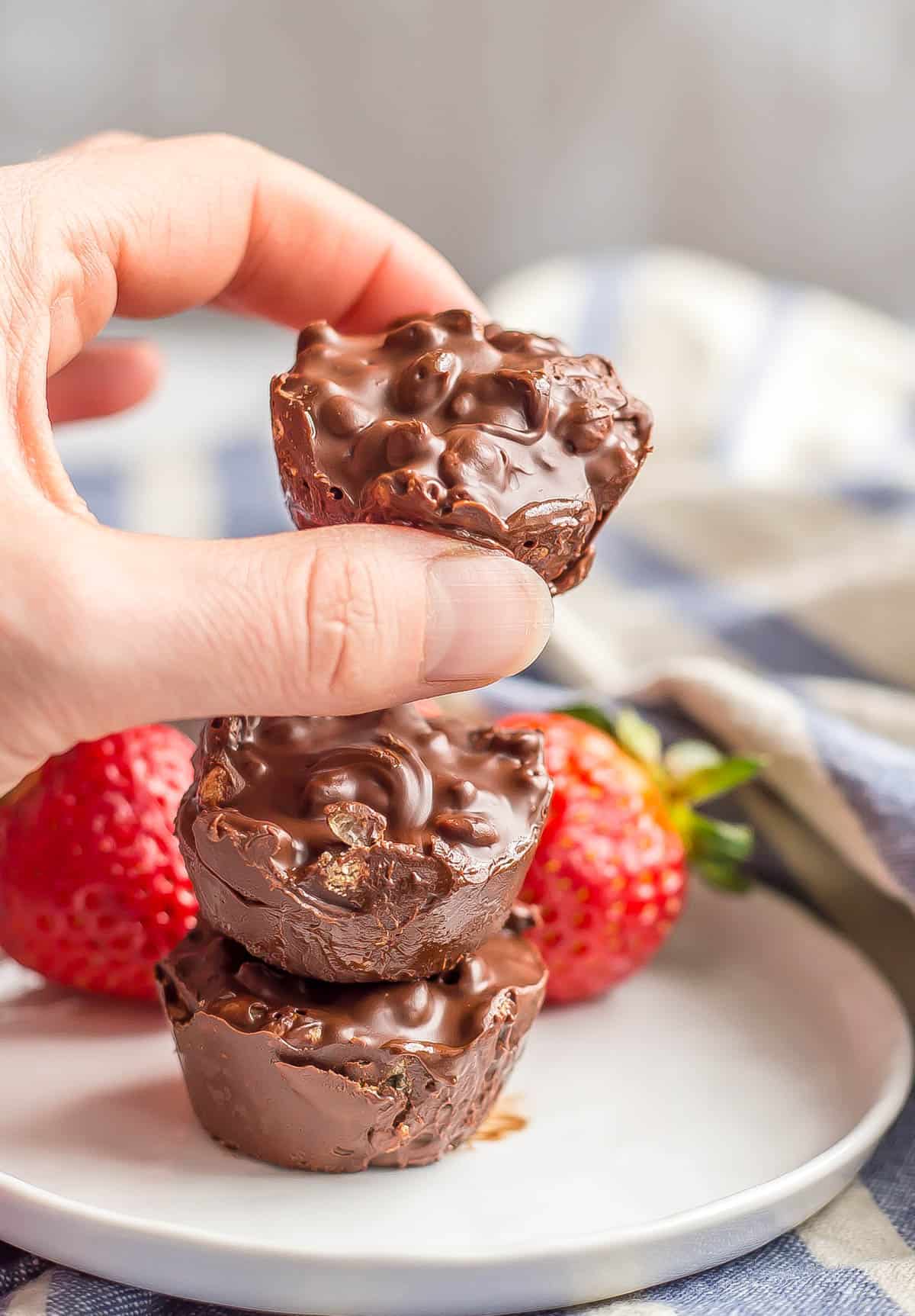 A hand picking up a homemade chocolate candy from a small stack on a little white plate.