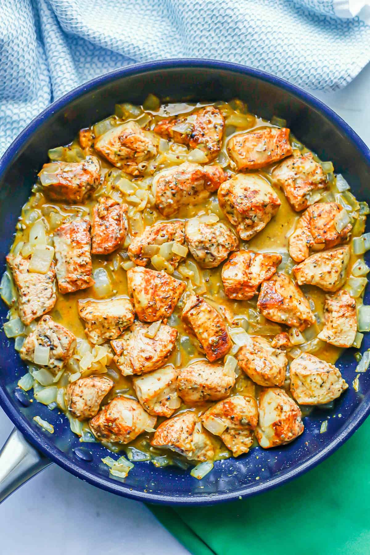 Cubed chicken pieces cooking in a large skillet with onions and a sauce.