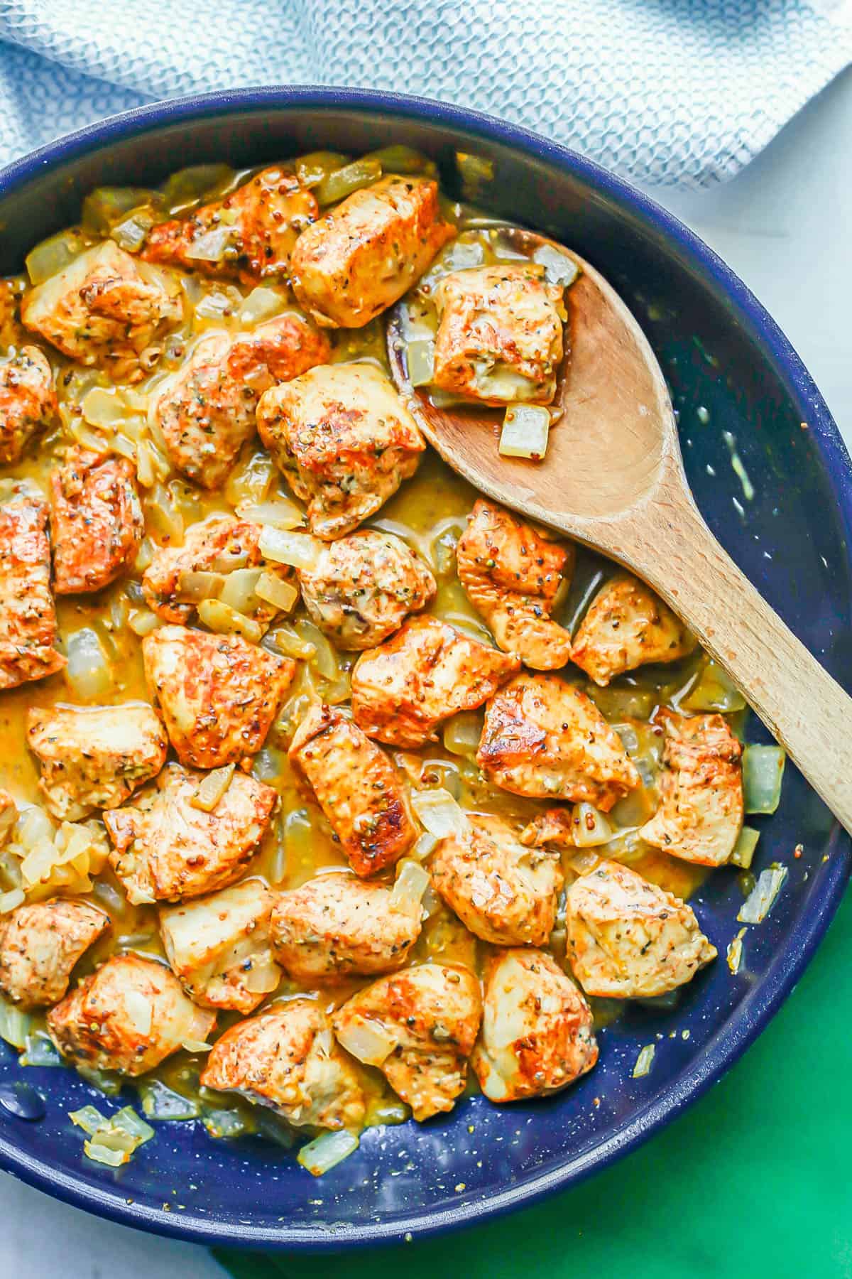 A wooden spatula resting in a skillet with a honey mustard chicken mixture.