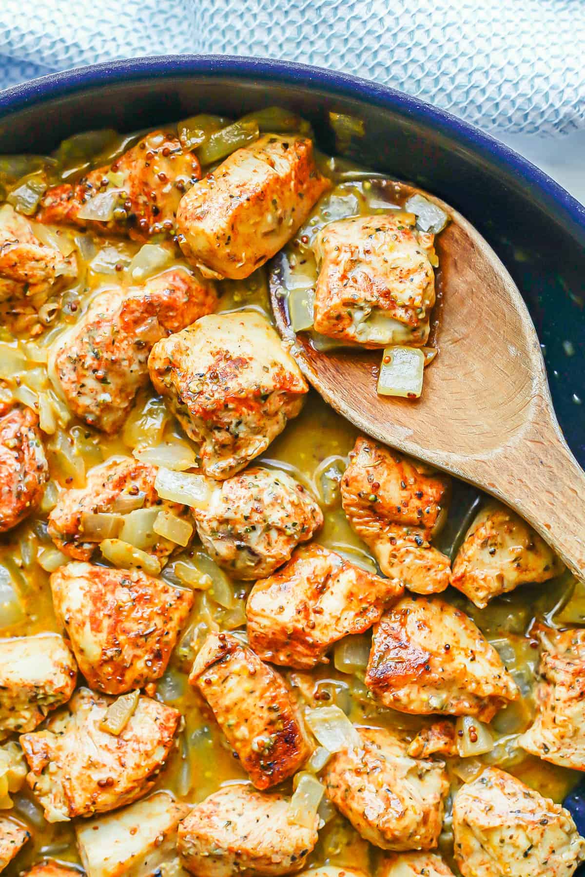 A wooden spoon in a skillet scooping up some honey mustard chicken.