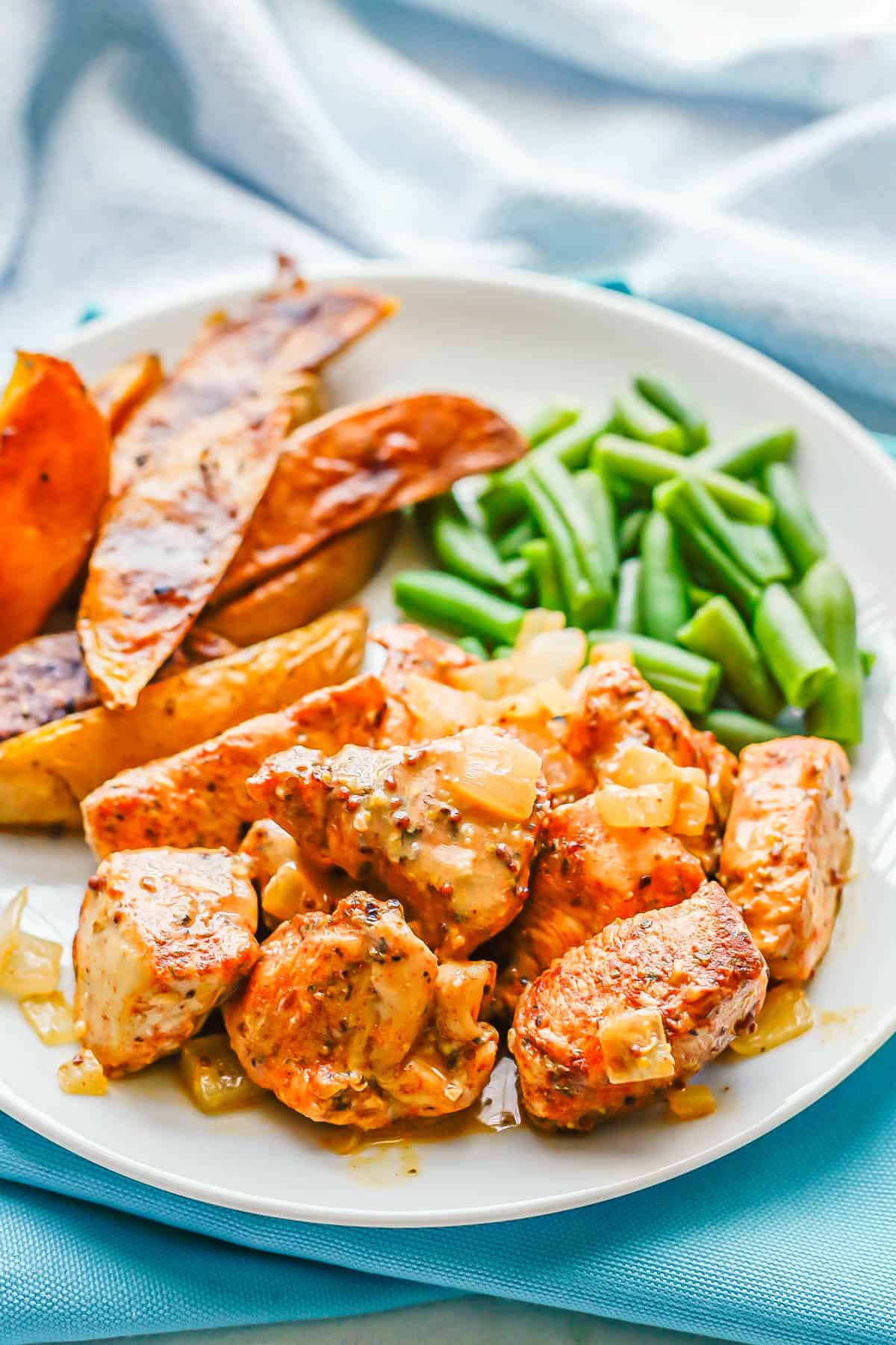 Cubed chicken served on a dinner plate with green beans and potato wedges.