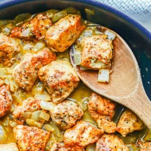 Close up of a wooden spoon in a skillet scooping up some honey mustard chicken.